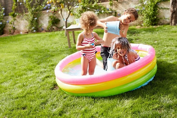 Drei Kinder spielen in einem Planschbecken.